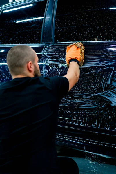 洗車シャンプー付きブラックラグジュアリーカーを洗浄するマイクロファイバー布を使用した洗車作業員のクローズアップ — ストック写真