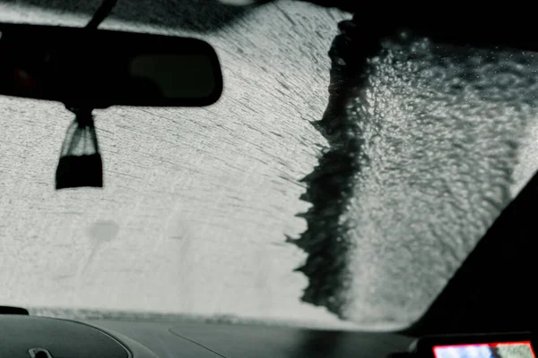 a close-up of the windshield and interior of a luxury car at the moment of car wash using foam and pressure washer