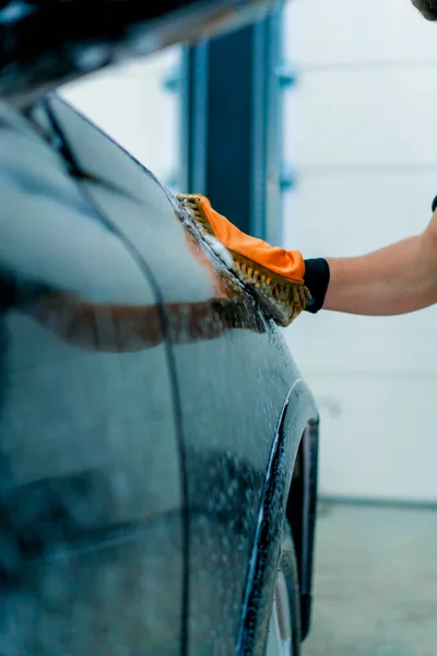 Close-up of a car wash worker using a microfiber cloth to wash black luxury car with car wash shampoo