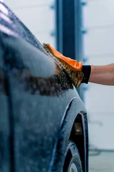 Close-up of a car wash worker using a microfiber cloth to wash black luxury car with car wash shampoo