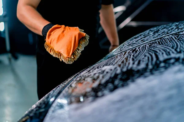 Close-up of a car wash worker using a microfiber cloth to wash black luxury car with car wash shampoo