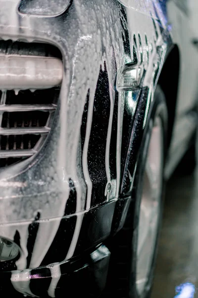 車の洗車ボックスに黒の高級車のフロントヘッドライトとバンパーの車の泡のクローズアップ — ストック写真