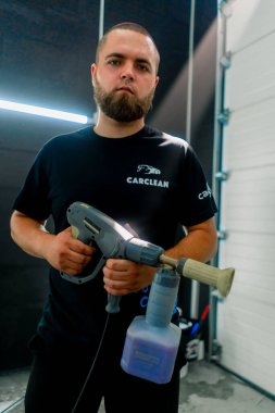 Araba yıkama işçisi sakallı, elinde köpük jeneratörü olan ciddi bir adamın portresi.