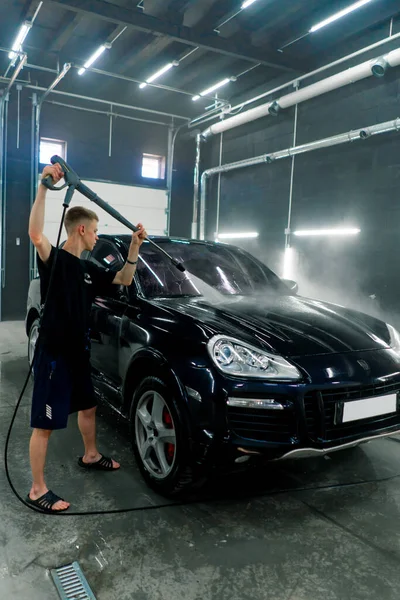 男性の洗車員が洗車場で高圧洗濯機で黒い高級車を洗浄する — ストック写真