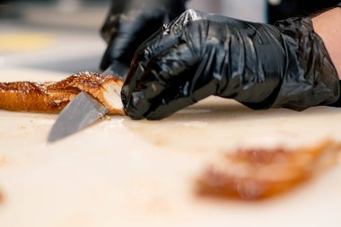 Eldivenli bir suşi şefinin mutfak masasında suşi yaparken profesyonel bıçakla yılan balığı filetosu keserken yakın plan fotoğrafı.