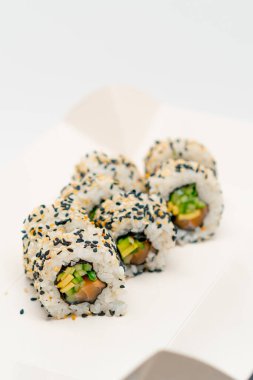 Salatalıklı mango pilavı ve beyaz arka planda susam olan somonlu California dürümünün yakın çekimi.