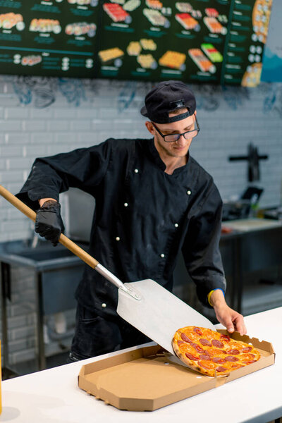 A pizzaiolo pulls a pizza from the oven with a pizza shovel and places it in pizza box in the pizzeria kitchen