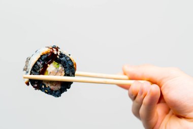 Sushi California 'ya yakın çekim. Siyah pirinç ve yılan balığıyla beyaz arka planda yemek çubukları olan bir adam.