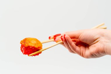 Karidesli fırında suşi ve yemek çubuklarıyla beyaz arka planda bir adamın eliyle tutulan yılan balığı.