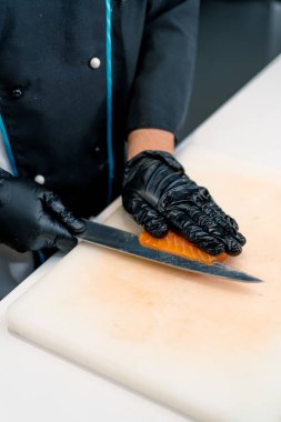Suşi restoranının mutfağında suşi hazırlarken somon filetosunu bıçakla kesen bir aşçının yakın çekimi.