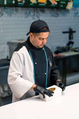 Bir suşi şefi suşi restoranının mutfağında sipariş vermek için suşi kutusuna California dürümü koyar.