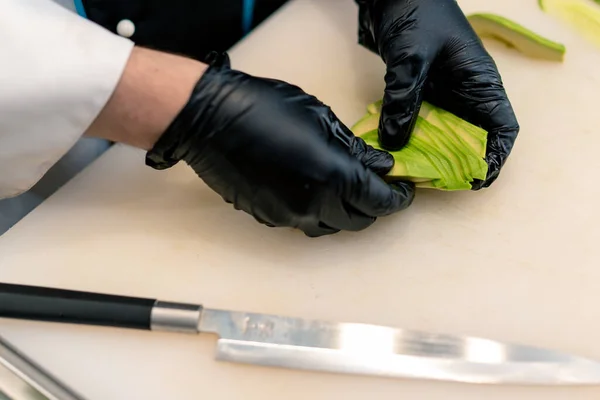 Primer Plano Fabricante Sushi Con Guantes Cortando Aguacate Con Cuchillo —  Fotos de Stock