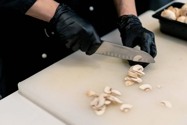 一名寿司制造商在专业厨房的白板上切蘑菇的手套特写 同时制作寿司 — 图库照片