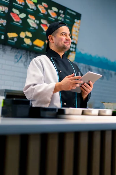 Przemyślane Sushi Chef Tabletką Rękach Pobliżu Stołu Kuchennego Którym Produkty — Zdjęcie stockowe