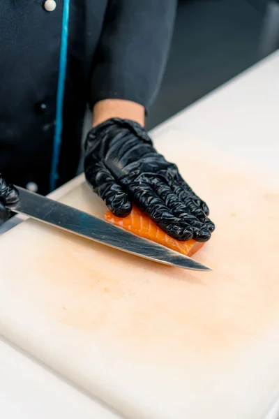 Close-up of a sushi chef cutting a salmon fillet with a knife while preparing sushi in the kitchen of sushi restaurant