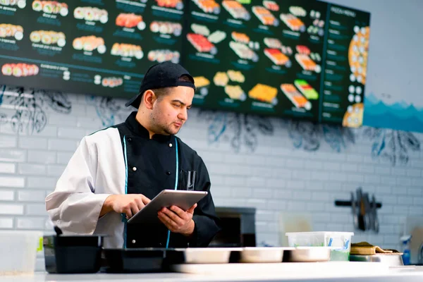 Zamyšlený Šéfkuchař Sushi Tabletou Rukou Kuchyňského Stolu Kterém Jsou Rozložené — Stock fotografie