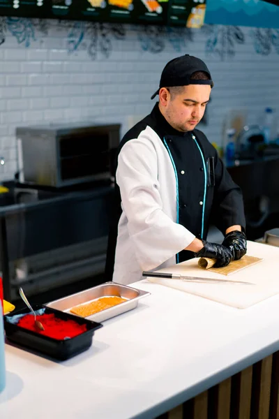ホワイトキッチンボードにシードサーモンクリームチーズとキュウリのフィラデルフィアロールを準備する過程でシェフ — ストック写真