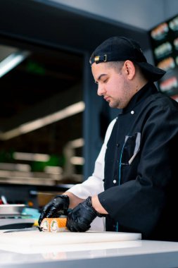 Suşi şefi, somon peyniri ve salatalıkla pişirdiği Philadelphia dürümünü suşi restoranının mutfağında bıçakla kesiyor.