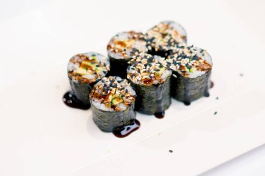 Unagi sosuna batırılmış avokadoyla yakın plan maki dürümleri ve suşi restoranının mutfağına susam tohumları serpiştirilmiş.