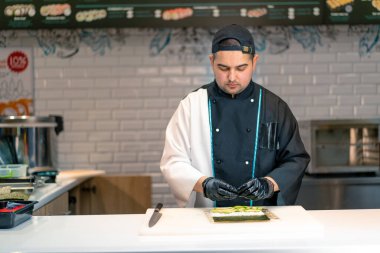 Bir suşi şefi suşi restoranının mutfağında suşi yapmak için nori avokado pilavı ve bambu hasırı kullanıyor.