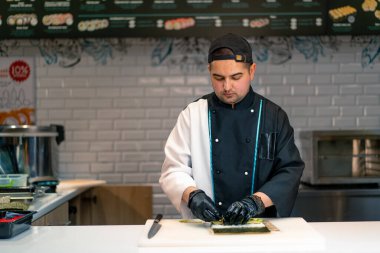 Bir suşi şefi suşi restoranının mutfağında suşi yapmak için nori avokado pilavı ve bambu hasırı kullanıyor.