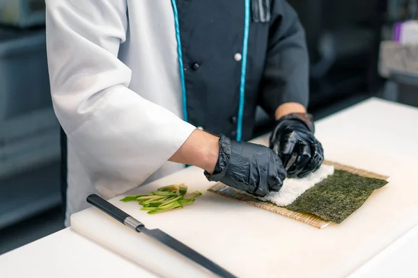 寿司シェフは 寿司屋の台所で寿司を作るために アボカドライスと竹マットを使用したメイクロールを準備します — ストック写真