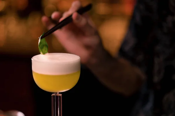 Close up of a bartender mixing a green cocktail on the bar into a cocktail glass at club bar