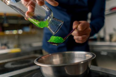 Profesyonel bir mutfakta yeşil havyar tanelerini kaşığa döken bir şefin yakın çekimi.