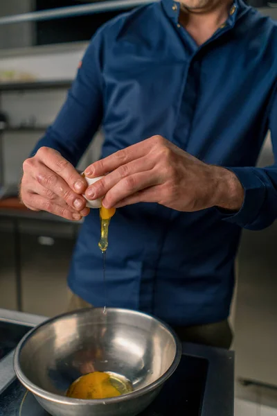 シェフはプロのキッチン卵黄クローズアップ調理でアイロンボウルに卵を分解します — ストック写真