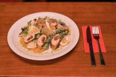 Kulüpteki bir barda, masada tavuklu ve yumurtalı Sezar salatasıyla beyaz bir tabağın yakın çekimi.