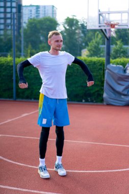 Uzun boylu basketbol oyuncusu antrenman başlamadan önce açık hava basketbol sahasında ısınıyor.