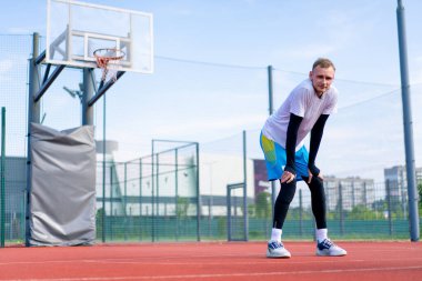 Uzun boylu basketbol oyuncusu antrenman başlamadan önce açık hava basketbol sahasında ısınıyor.