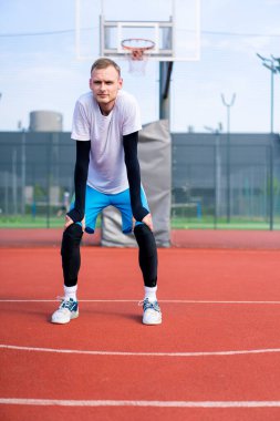 Uzun boylu basketbol oyuncusu antrenman başlamadan önce açık hava basketbol sahasında ısınıyor.