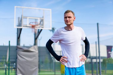 Uzun boylu basketbol oyuncusu antrenman başlamadan önce açık hava basketbol sahasında ısınıyor.