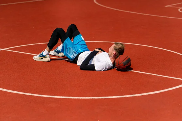 Tall guy basketball player lying on a basketball court in the park along with  basketball resting during practice