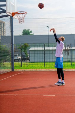Uzun boylu basketbolcu antrenman sırasında parkta basketbol sahasında basket potasına top atıyor.