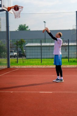 Uzun boylu basketbolcu antrenman sırasında parkta basketbol sahasında basket potasına top atıyor.