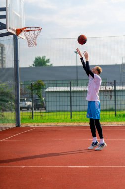 Uzun boylu basketbolcu antrenman sırasında parkta basketbol sahasında basket potasına top atıyor.