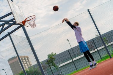 Uzun boylu basketbolcu antrenman sırasında parkta basketbol sahasında basket potasına top atıyor.