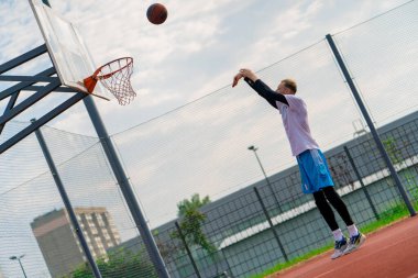 Uzun boylu basketbolcu antrenman sırasında parkta basketbol sahasında basket potasına top atıyor.