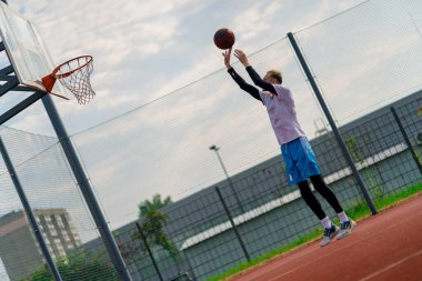 Uzun boylu basketbolcu antrenman sırasında parkta basketbol sahasında basket potasına top atıyor.