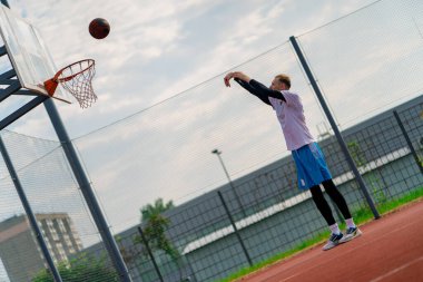 Uzun boylu basketbolcu antrenman sırasında parkta basketbol sahasında basket potasına top atıyor.