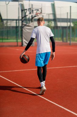 Uzun boylu basketbol oyuncusu parktaki basketbol sahasında top sürme yeteneğini gösteriyor.