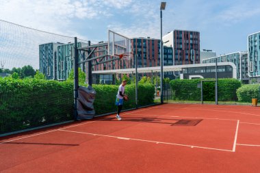 Uzun boylu basketbol oyuncusu parktaki basketbol sahasında top sürme yeteneğini gösteriyor.