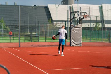 Uzun boylu basketbol oyuncusu parktaki basketbol sahasında top sürme yeteneğini gösteriyor.