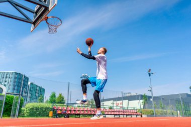 Uzun boylu basketbolcu elinde topla potaya atlıyor. Park 'taki basketbol sahasında yaptığı antrenmanda muhteşem bir smaç yapmak için.