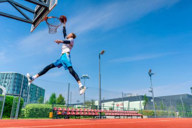 Uzun boylu basketbolcu elinde topla potaya atlıyor. Park 'taki basketbol sahasında yaptığı antrenmanda muhteşem bir smaç yapmak için.