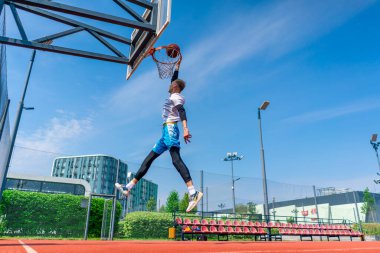 Uzun boylu basketbolcu elinde topla potaya atlıyor. Park 'taki basketbol sahasında yaptığı antrenmanda muhteşem bir smaç yapmak için.
