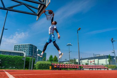 Uzun boylu basketbolcu elinde topla potaya atlıyor. Park 'taki basketbol sahasında yaptığı antrenmanda muhteşem bir smaç yapmak için.
