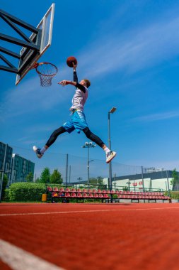 Uzun boylu basketbolcu elinde topla potaya atlıyor. Park 'taki basketbol sahasında yaptığı antrenmanda muhteşem bir smaç yapmak için.